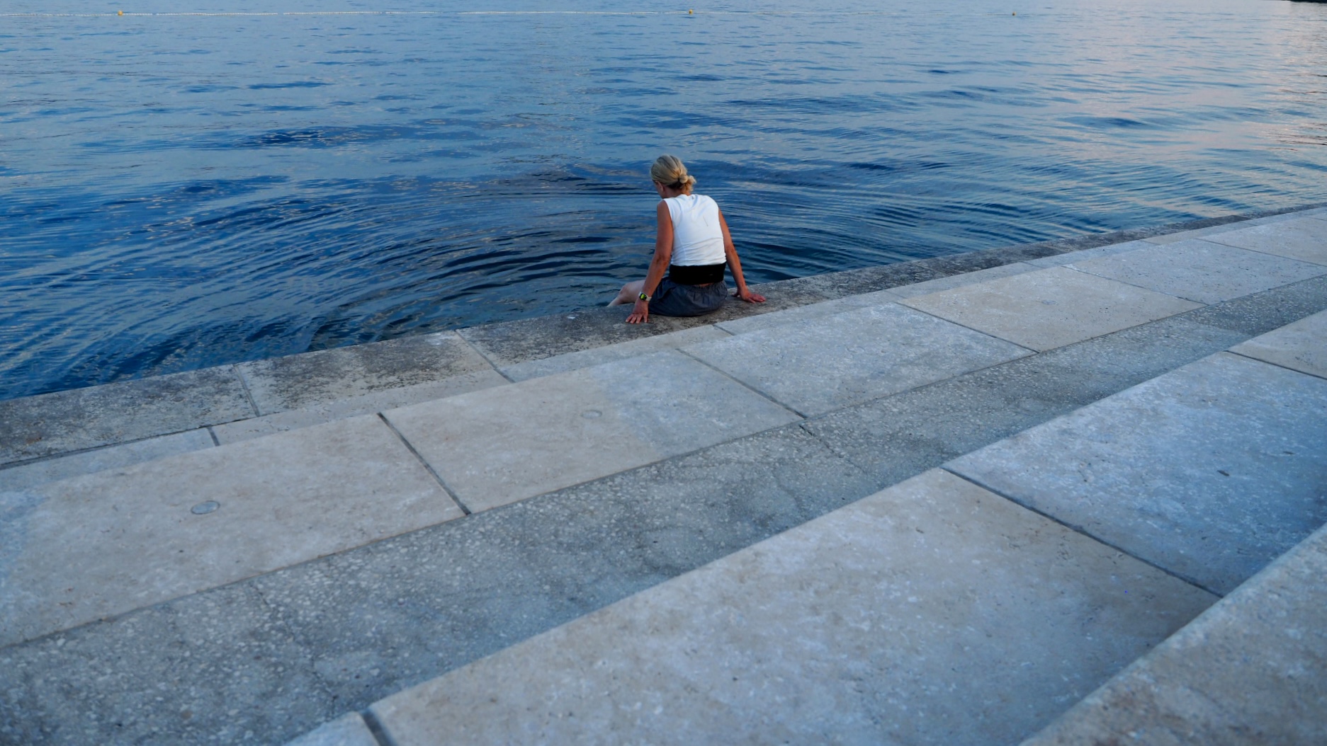Angie sitzt am Wasser auf einer steinernen Kaimauer vor Rovinj.